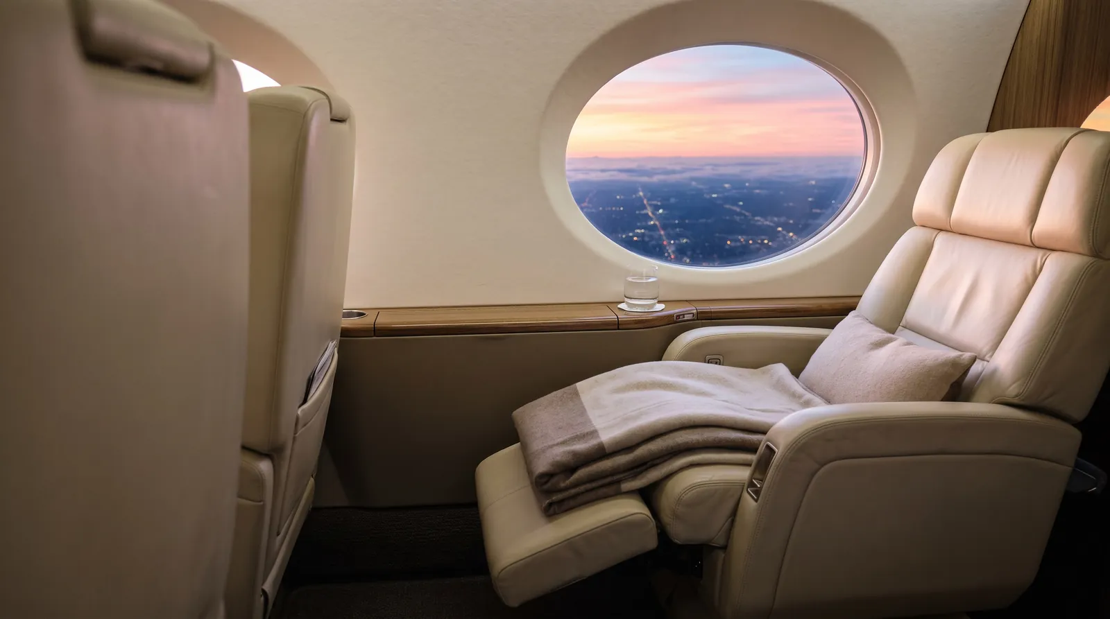 Reclined seat and glass of water by a business jet window at sunrise