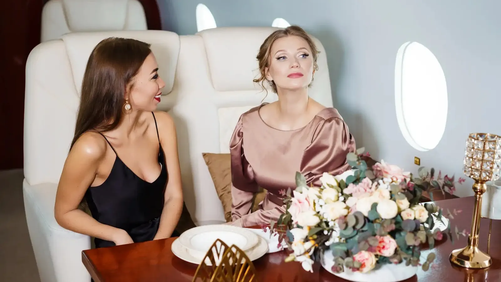Two passengers at a table laid with flowers and plates in a private jet cabin