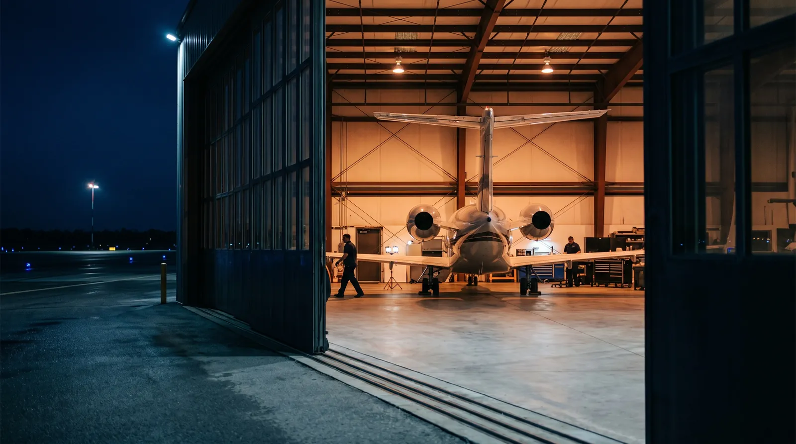 A private jet in a lit hangar seen through a half open door at night